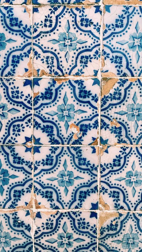 Blauwe en witte keramische tegels met ingewikkelde geometrische en bloemmotieven, die tekenen van slijtage, barsten en afgebladderde randen vertonen - een klassieke Lissabon must voor wie op zoek is naar verouderde en verweerde charme.