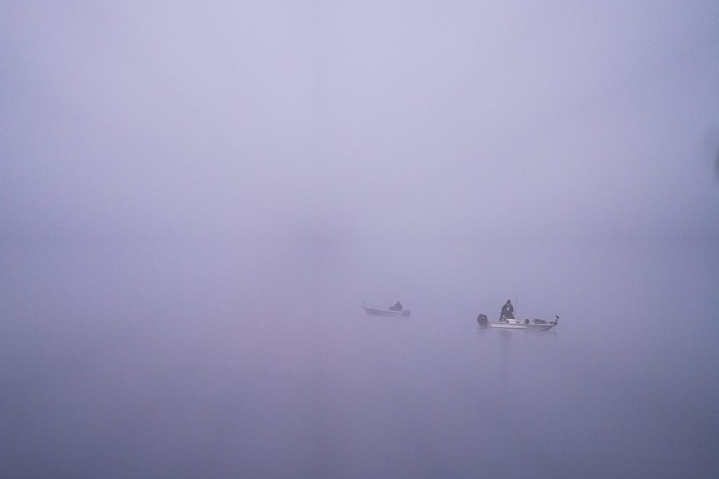 Twee kleine boten dobberen op kalm water omgeven door dichte mist in Zweden, met zwakke reflecties en weinig zichtbare details, waardoor een serene en mysterieuze sfeer ontstaat.