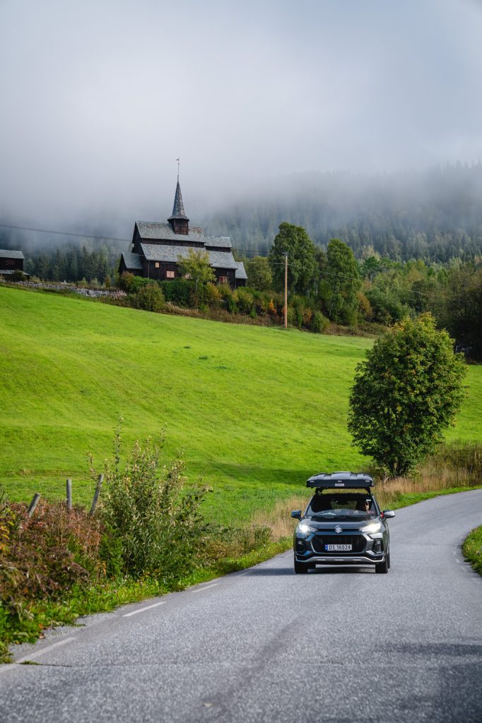 Een auto rijdt over een weg met fjorden op de achtergrond, de geest van Noorwegen Nomads vastleggend onder de betoverende gloed van de middernachtzon.