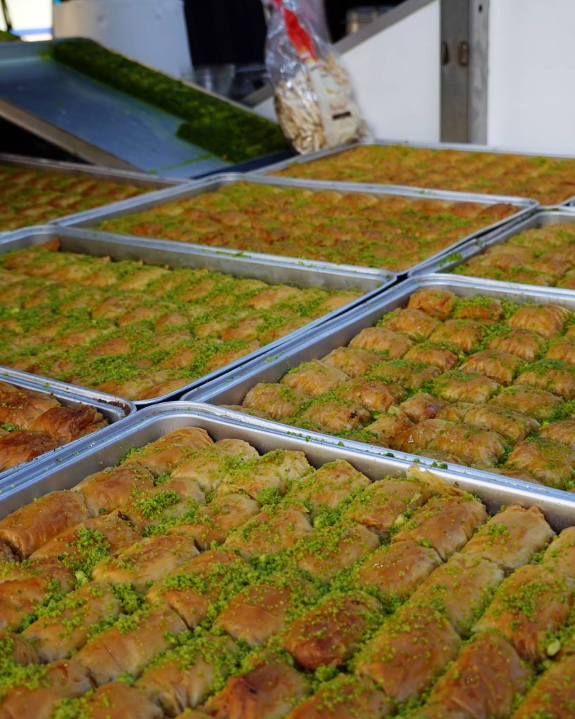 Dienbladen gevuld met rijen baklava overgoten met gemalen pistachenoten, uitgestald op een markt of bakkerij, tonen echte Genkse Gastvrijheid.