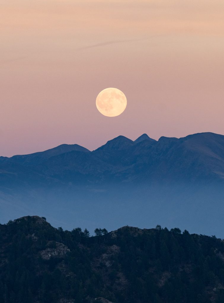De volle oogstmaan staat boven blauwe bergkammen in Ticino, gezien vanaf de Monte Gambarogno bij zonsondergang.