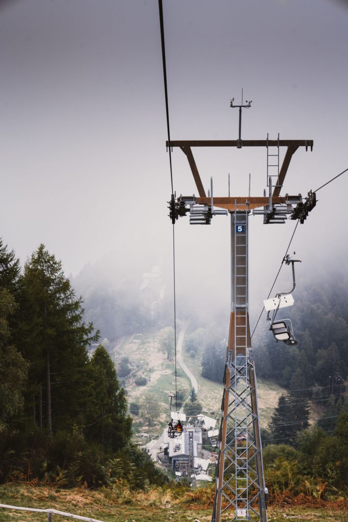 De stoeltjeslift van Cardada naar Cimetta verdwijnt in de mist, met een mast en lege stoeltjes boven het bos.