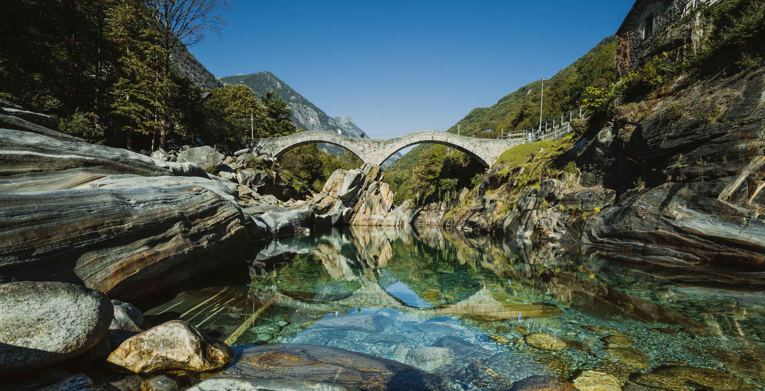 De Ponte dei Salti, de stenen brug met twee bogen in Lavertezzo, weerspiegelt in het heldere water van de Verzasca.